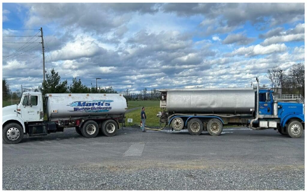 Two large tanker trucks parked side by side on a rural highway under a partly cloudy sky.